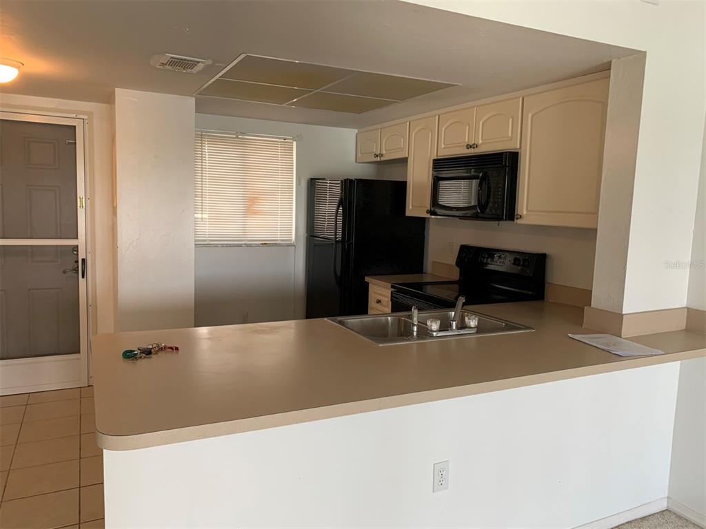 A kitchen features light-colored cabinets, black appliances, and a peninsula with a sink — 25275 RAMPART BOULEVARD UNIT 1306, PUNTA GORDA, FL
