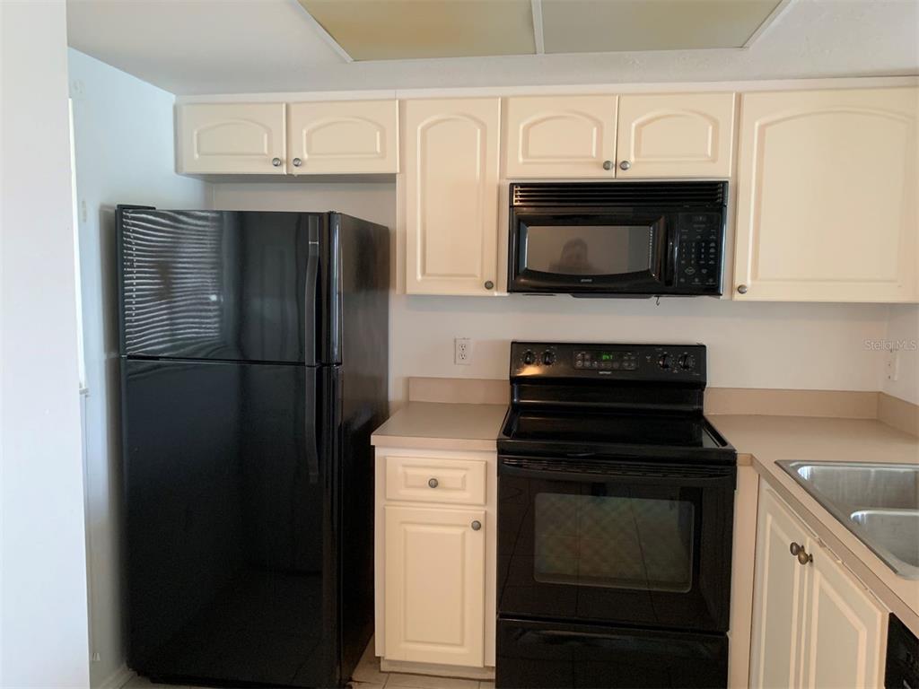 A kitchen features white cabinets, black appliances, and light-colored countertops — 25275 RAMPART BOULEVARD UNIT 1306, PUNTA GORDA, FL