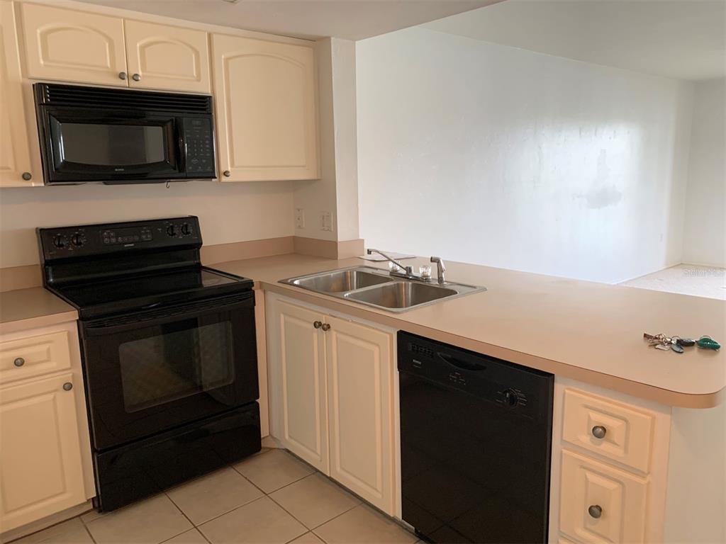 A kitchen features white cabinets, black appliances, a double sink, and beige countertops — 25275 RAMPART BOULEVARD UNIT 1306, PUNTA GORDA, FL