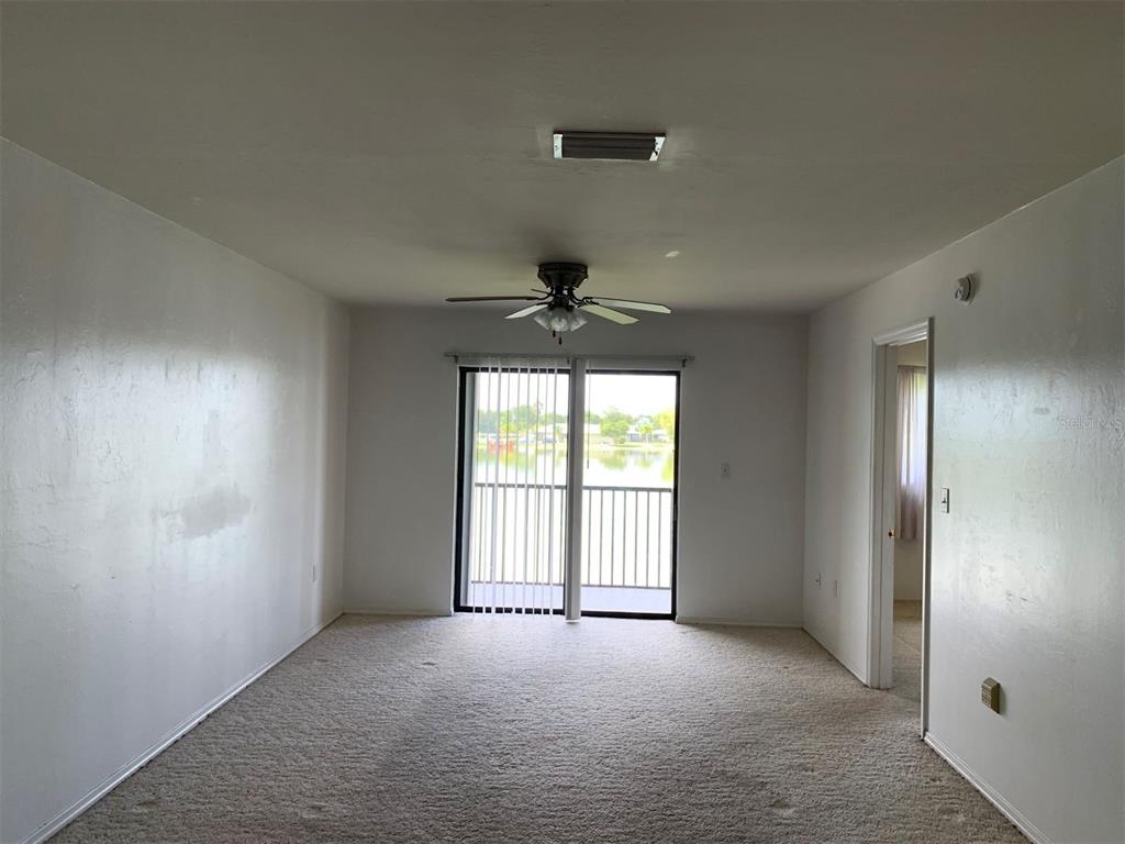 A living room with beige carpet, white walls, a ceiling fan, and a sliding glass door — 25275 RAMPART BOULEVARD UNIT 1306, PUNTA GORDA, FL