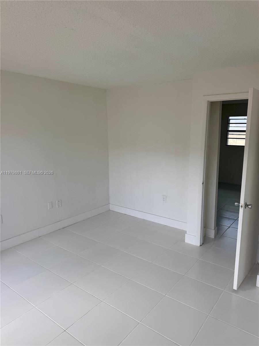 An empty room features white walls, light-colored tile flooring, and an open doorway — 1077 NW 45th Ave # 0, Miami FL 33126, MIAMI, FL