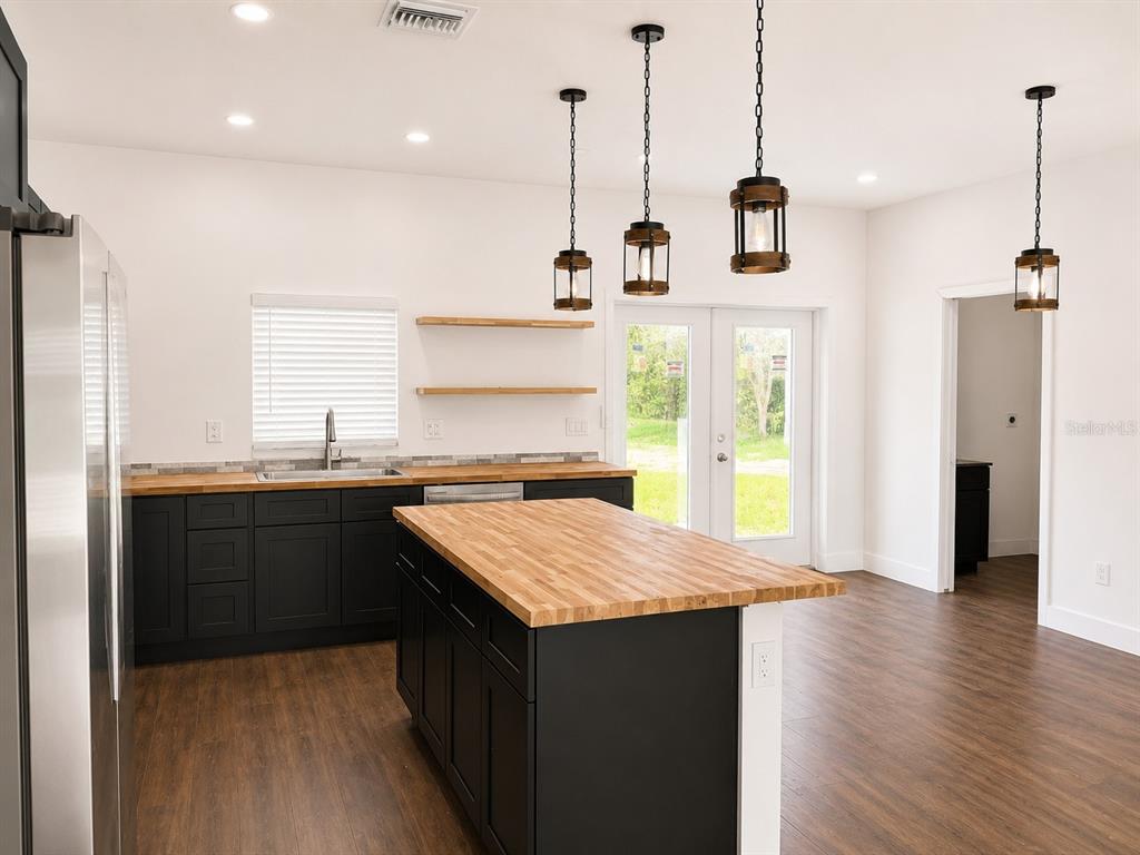 A kitchen with black cabinets, a wood-topped island, and pendant lighting over a wood floor — 16848 NW 288TH STREET, OKEECHOBEE, FL