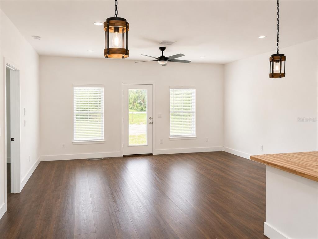 A living room features dark wood-look flooring, white walls, a ceiling fan, and pendant lighting — 16848 NW 288TH STREET, OKEECHOBEE, FL