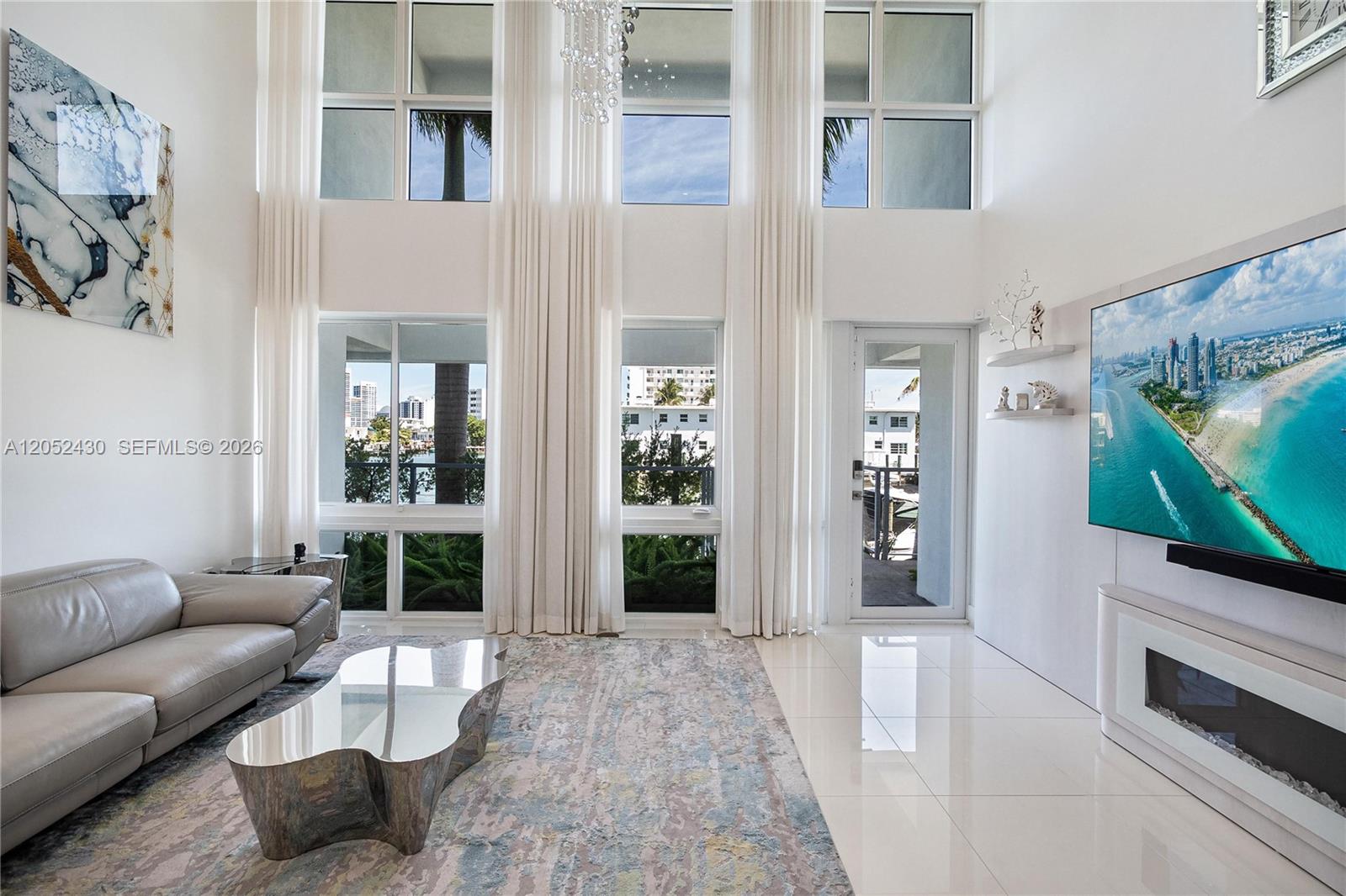 A modern living room features double-height windows, white tile floors, and a large wall-mounted television — 31 N Shore Dr # 31, Miami Beach FL 33141, MIAMI BEACH, FL