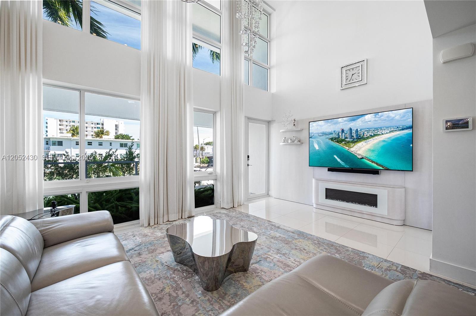 A modern living room features high ceilings, floor-to-ceiling windows, a wall-mounted television, and tile flooring — 31 N Shore Dr # 31, Miami Beach FL 33141, MIAMI BEACH, FL