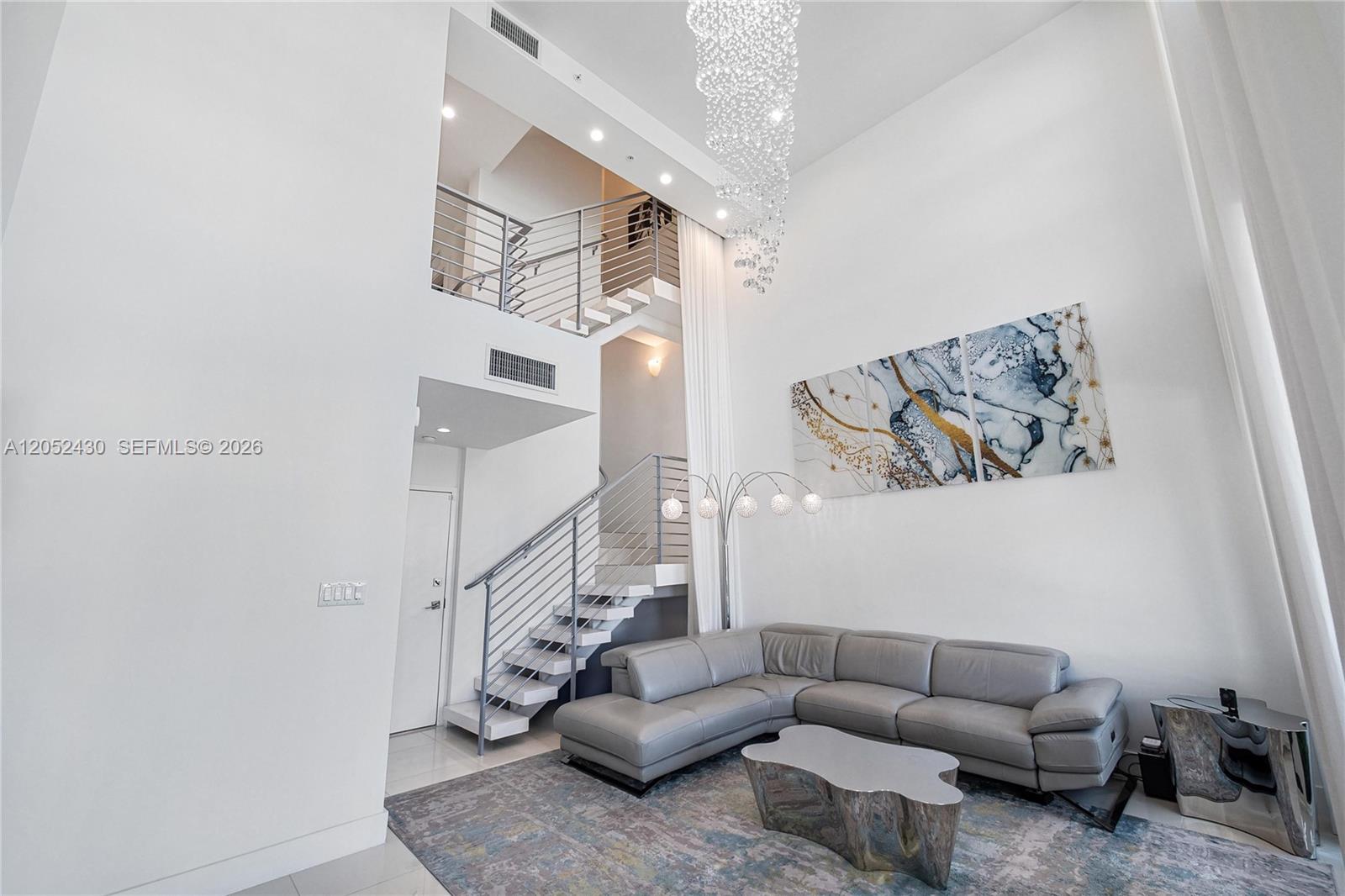 A modern living room features a high ceiling, a grey sectional sofa, and a staircase — 31 N Shore Dr # 31, Miami Beach FL 33141, MIAMI BEACH, FL