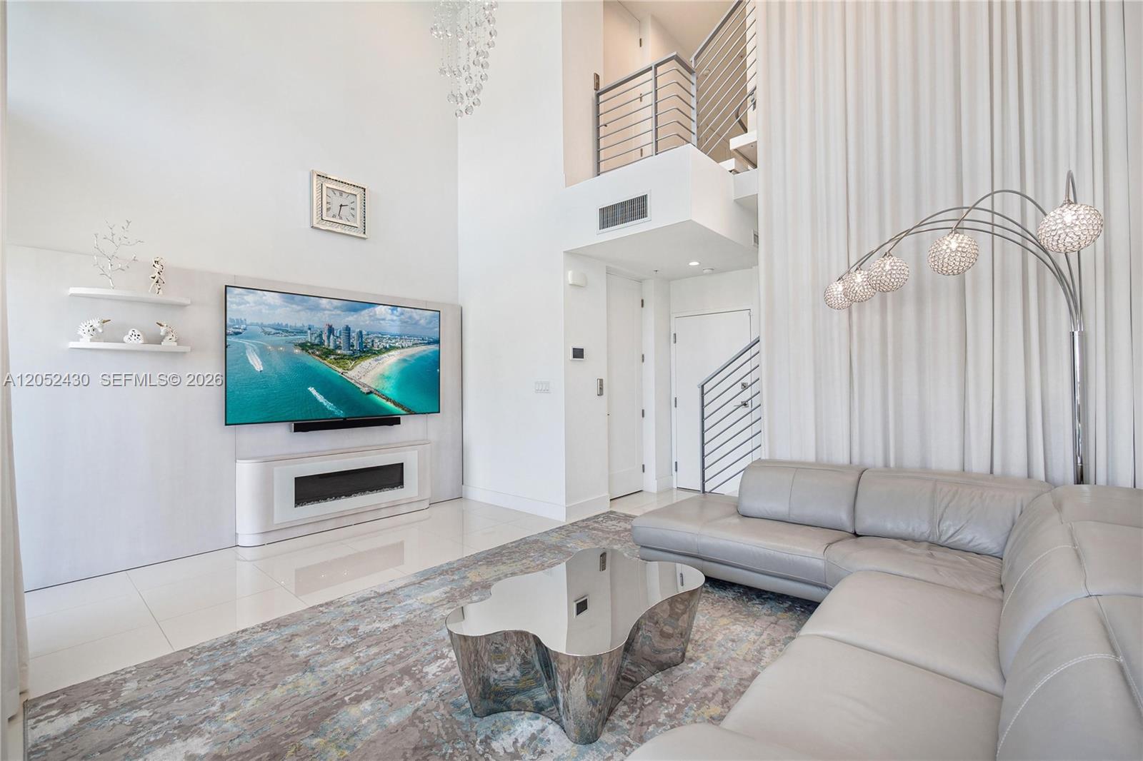 A modern living room features a high ceiling, a large television, and a sectional sofa — 31 N Shore Dr # 31, Miami Beach FL 33141, MIAMI BEACH, FL