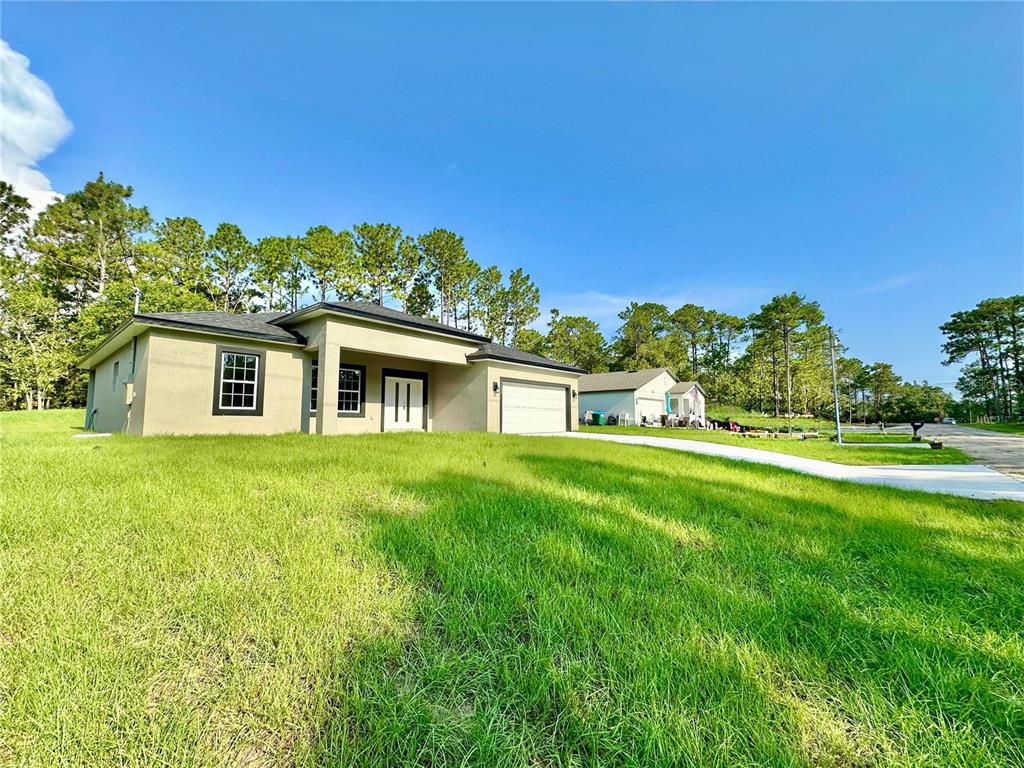 A single-story house with a beige stucco exterior, a two-car garage, and a grassy lawn — 6682 N EDELWEISS WAY, CITRUS SPRINGS, FL