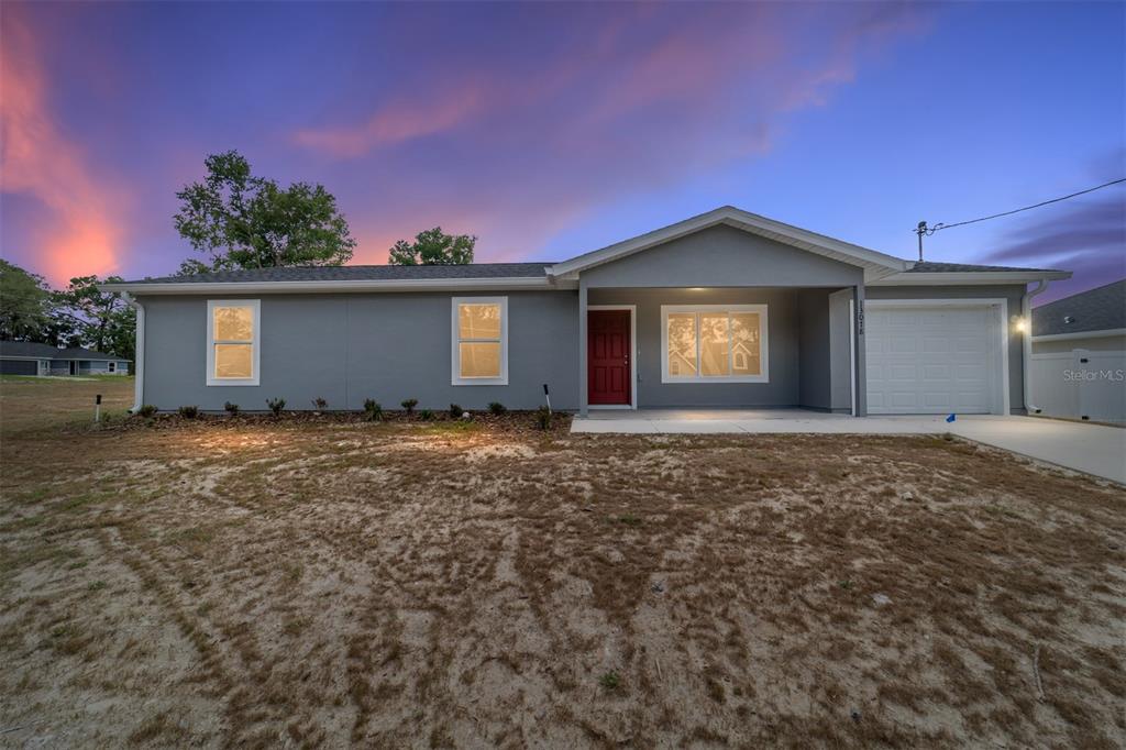 A single-story gray house with a red front door and a one-car garage at sunset — 13078 NE 7TH LOOP, SILVER SPRINGS, FL