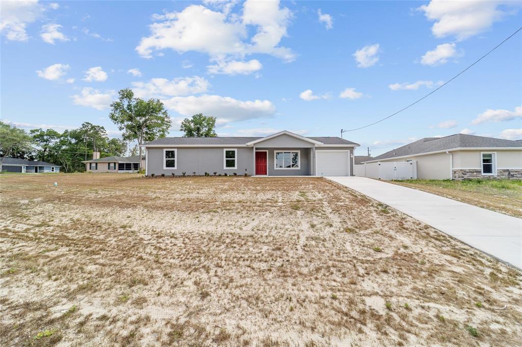 A single-story house with a red front door and a concrete driveway sits on land — 13078 NE 7TH LOOP, SILVER SPRINGS, FL