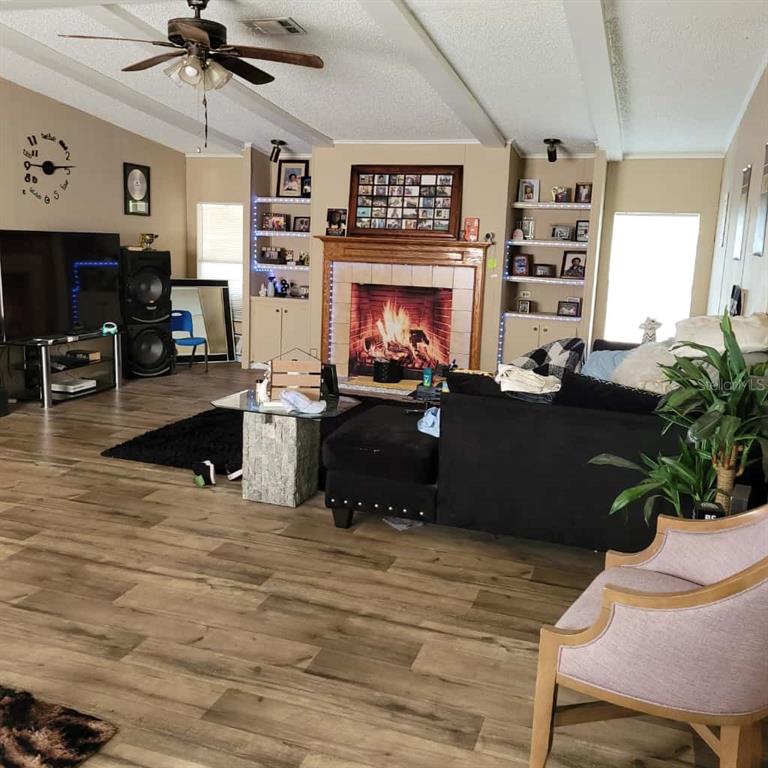A living room features wood-look flooring, a fireplace with built-in shelving, and a ceiling fan — 16165 NARROW STREET, BROOKSVILLE, FL