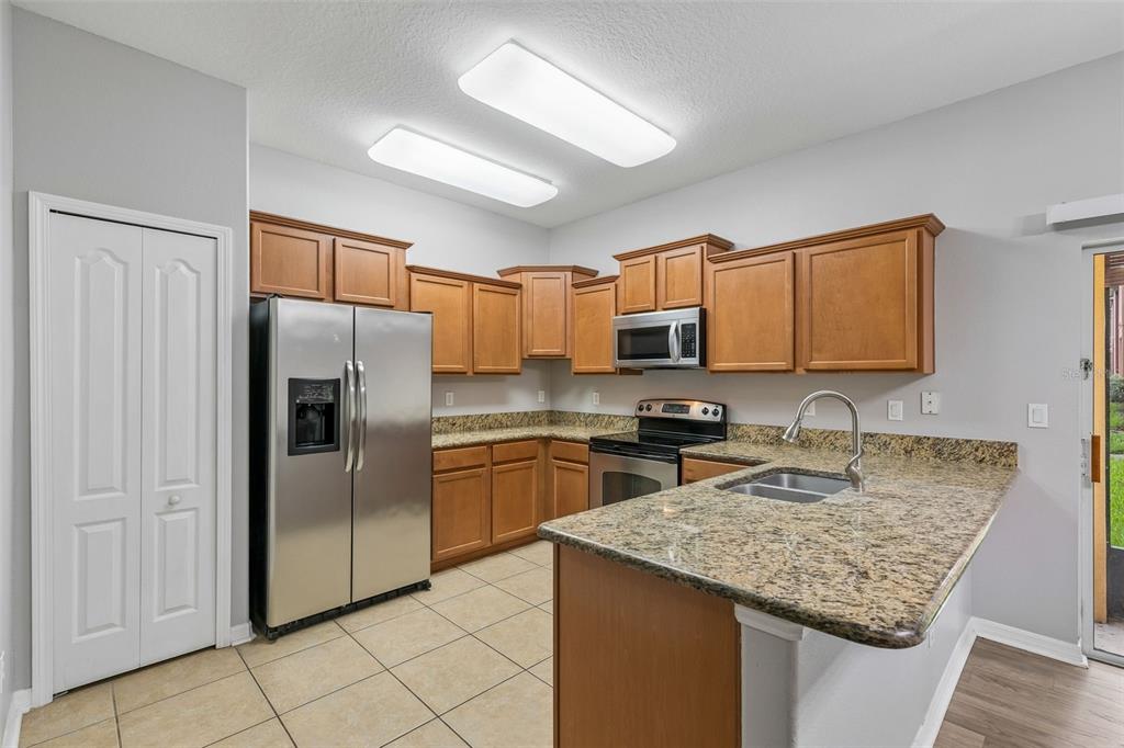A kitchen features wood cabinets, granite countertops, stainless steel appliances, and light-colored tile flooring — 1220 TWIN TREES LANE, SANFORD, FL