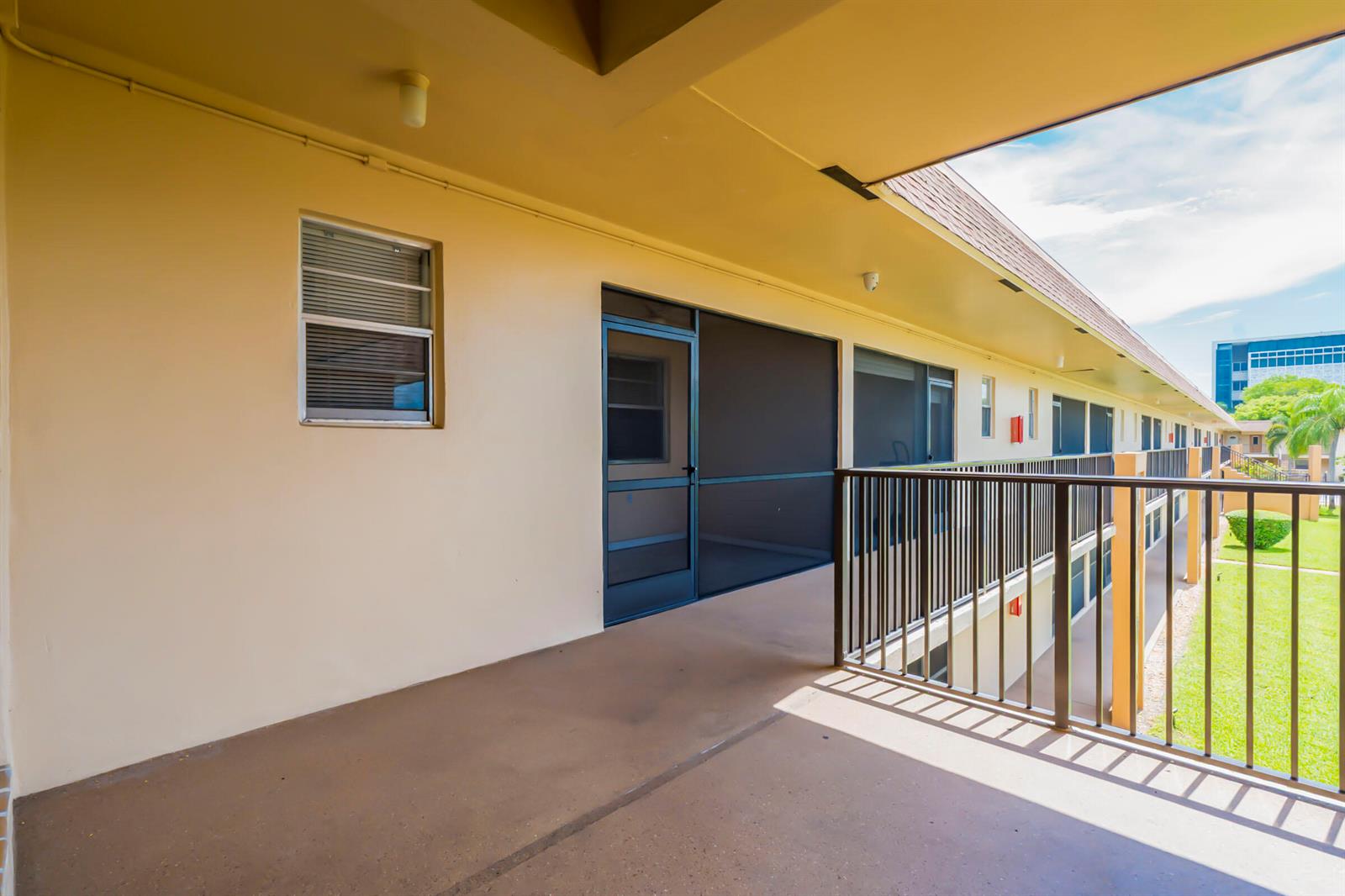 An outdoor covered walkway features a beige wall, a screened door, and a metal railing — 421 NE 1ST Street # 204, Hallandale Beach FL 33009, HALLANDALE BEACH, FL