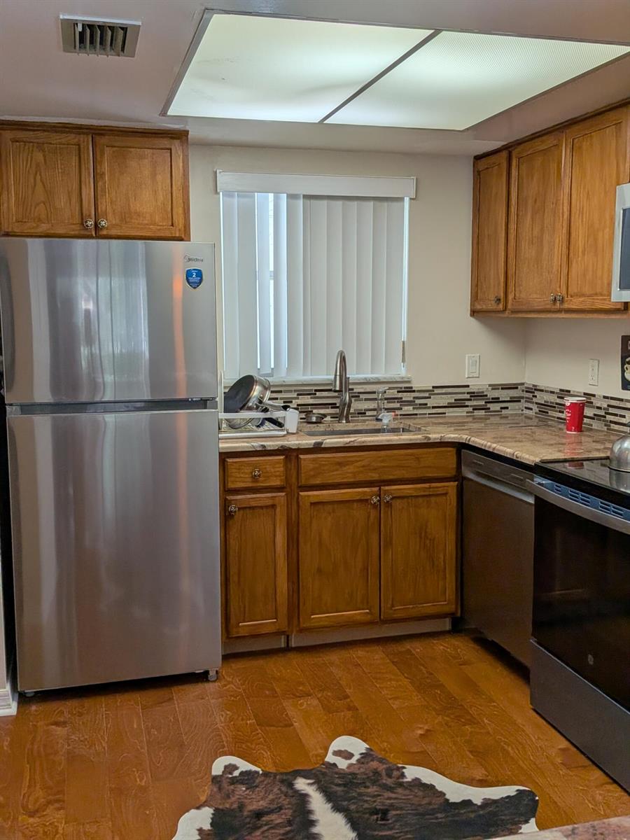 A kitchen with wood cabinets, stainless steel appliances, a tiled backsplash, and hardwood flooring — 4141 16th Street, Vero Beach FL 32960, VERO BEACH, FL