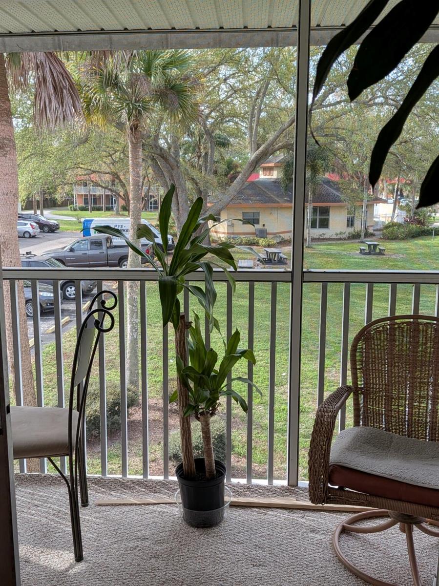 A screened-in balcony features a potted plant, two chairs, and a view of a parking lot — 4141 16th Street, Vero Beach FL 32960, VERO BEACH, FL