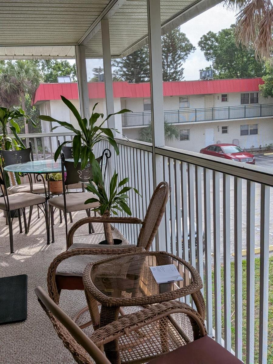 A screened-in balcony features wicker furniture, potted plants, and a view of an apartment building — 4141 16th Street, Vero Beach FL 32960, VERO BEACH, FL