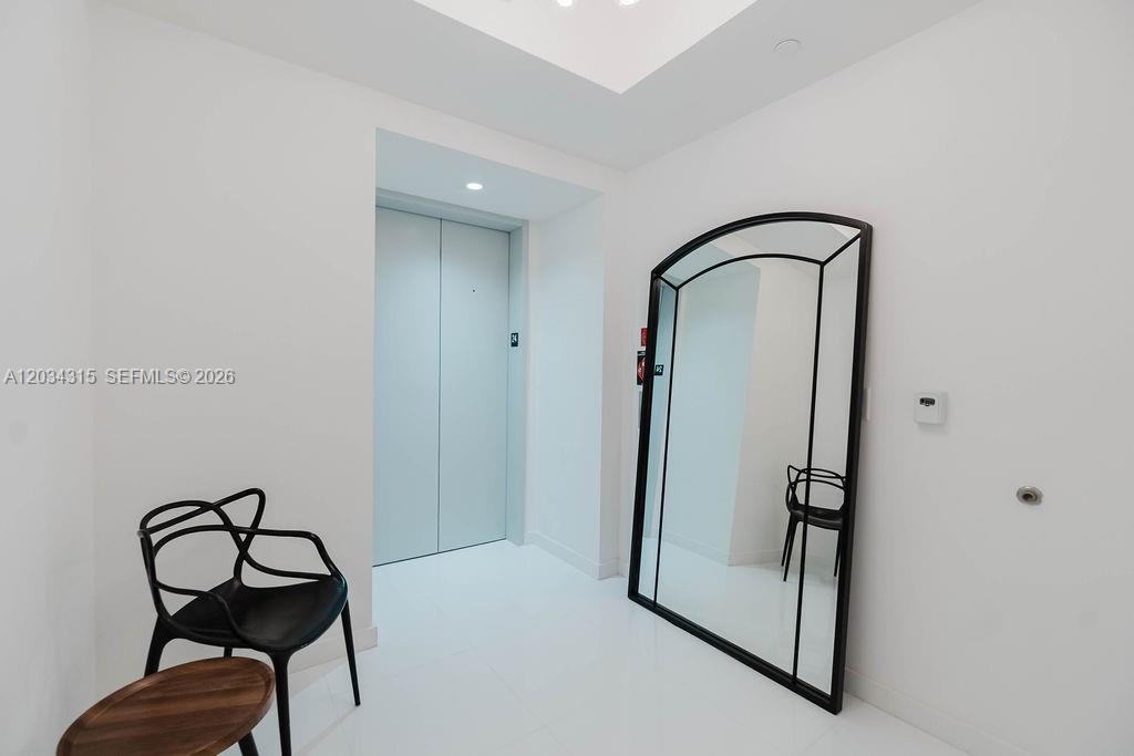 A minimalist entryway features white walls, a large arched mirror, and a black chair — 851 NE 1st Ave # 2403, Miami FL 33132, MIAMI, FL