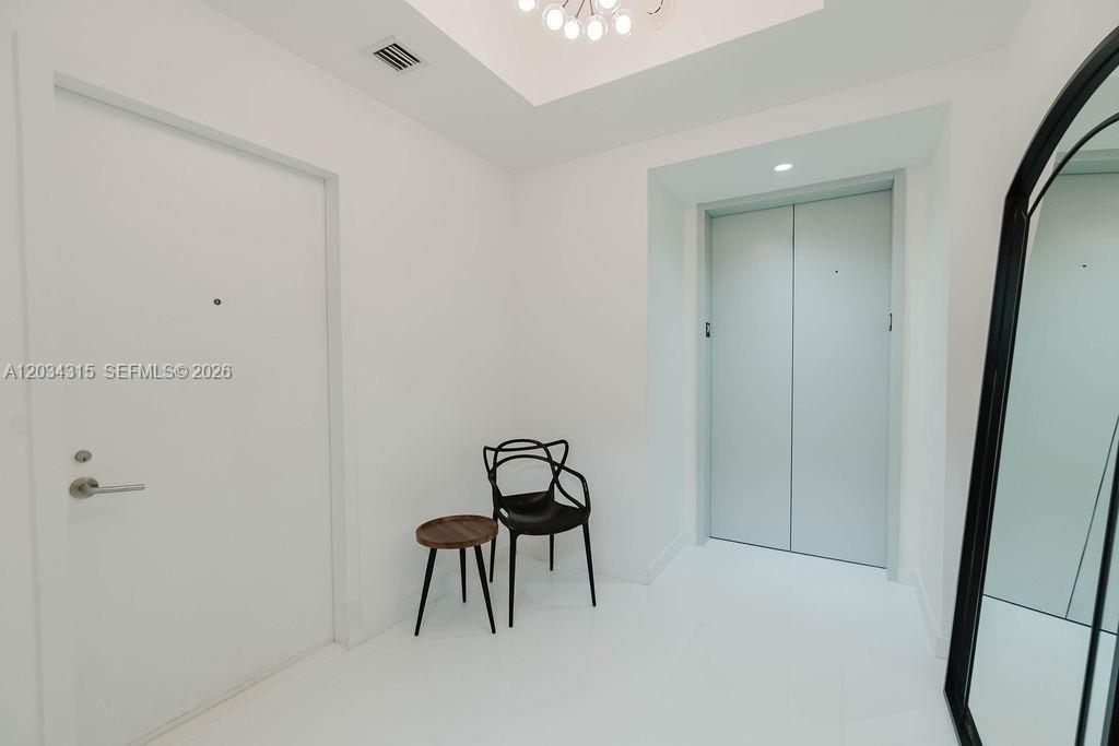 A minimalist white entryway features a black chair, a small side table, and double doors — 851 NE 1st Ave # 2403, Miami FL 33132, MIAMI, FL