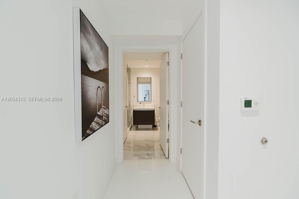 A white hallway leads to a bathroom with a vanity and marble-style flooring — 851 NE 1st Ave # 2403, Miami FL 33132, MIAMI, FL