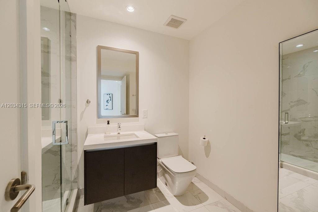A modern bathroom features a glass-enclosed shower, a dark wood vanity, and white tile flooring — 851 NE 1st Ave # 2403, Miami FL 33132, MIAMI, FL