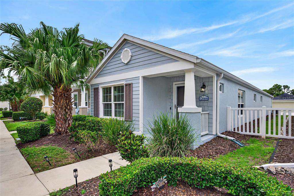 A light blue single-story house features a palm tree, a front porch, and white fencing — 12666 SHIMMERING OAK CIRCLE, VENICE, FL