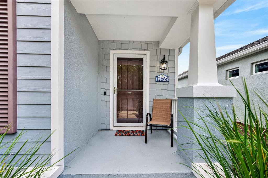 A covered front porch features light blue siding, a storm door, and a single chair — 12666 SHIMMERING OAK CIRCLE, VENICE, FL