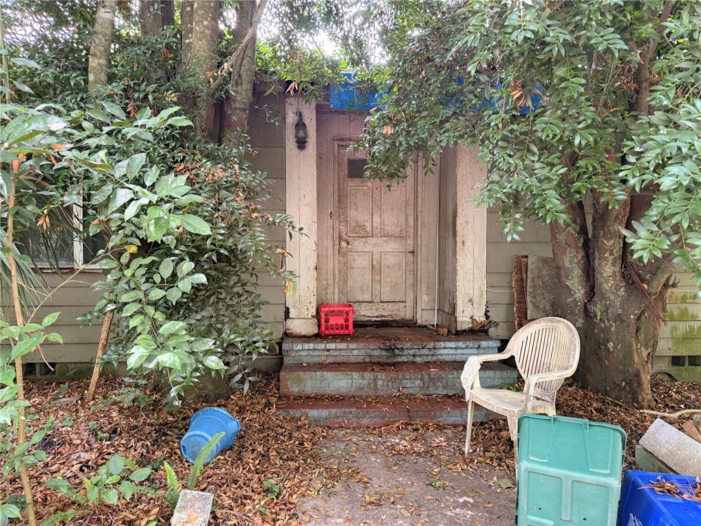 An exterior view of a weathered house entrance with a wooden door and brick steps — 1804 S MAPLE AVENUE, SANFORD, FL