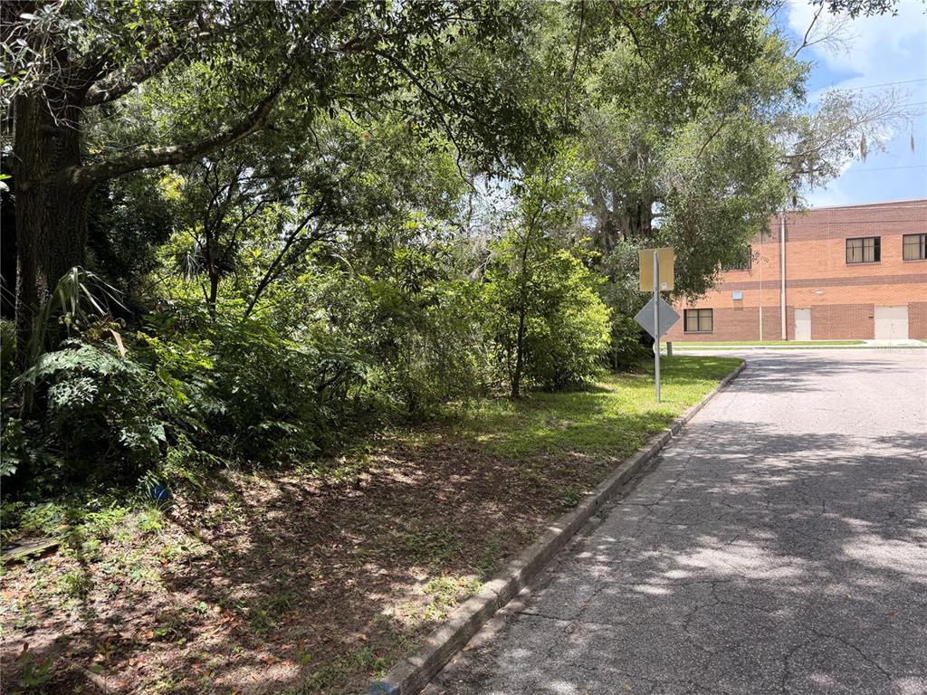 A paved road leads past a wooded lot toward a brick commercial building — 1804 S MAPLE AVENUE, SANFORD, FL