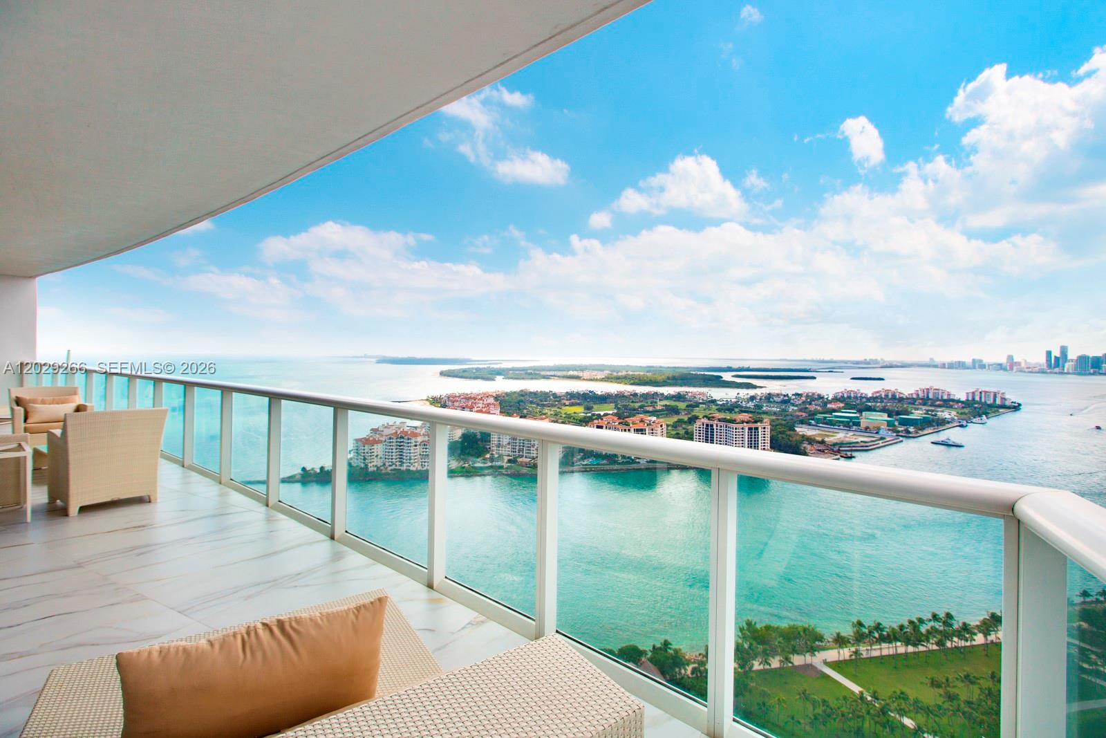 A balcony with light-colored tile flooring overlooks a bay with islands and a city skyline — 100 S Pointe Dr # 3701, Miami Beach FL 33139, MIAMI BEACH, FL