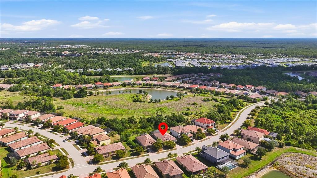 An aerial view shows a suburban neighborhood with houses, a central pond, and surrounding greenery — 12540 CANAVESE LANE, VENICE, FL