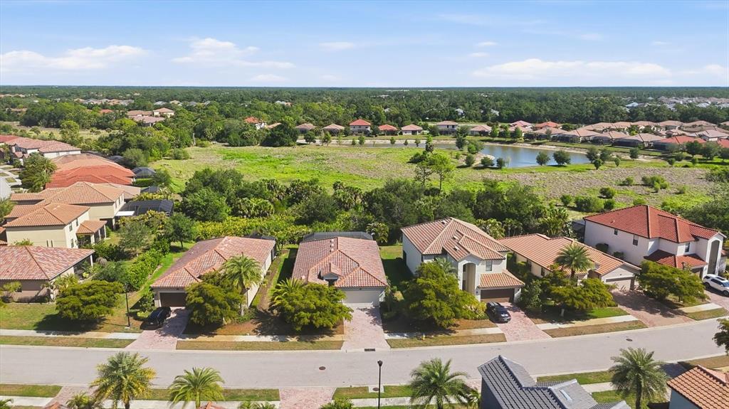 An aerial view shows a suburban neighborhood with houses, a pond, and green space — 12540 CANAVESE LANE, VENICE, FL
