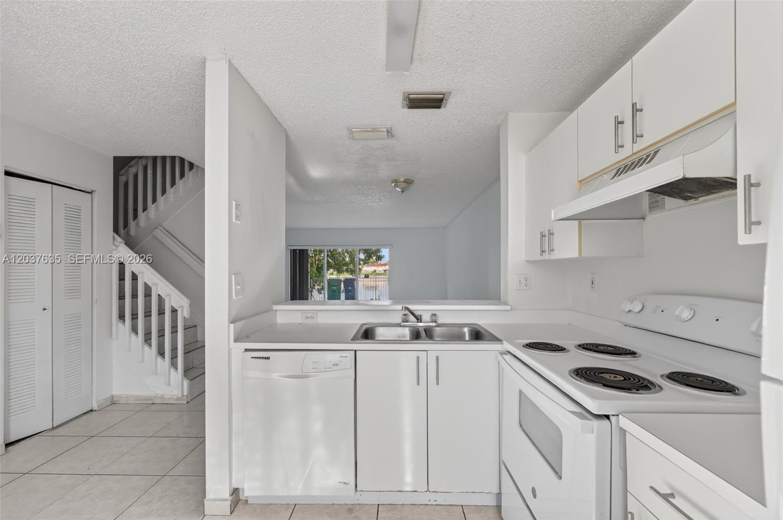 A white kitchen features a double sink, dishwasher, and electric stove, opening to a living area — 17378 SW 139th Ct, Miami FL 33177, MIAMI, FL