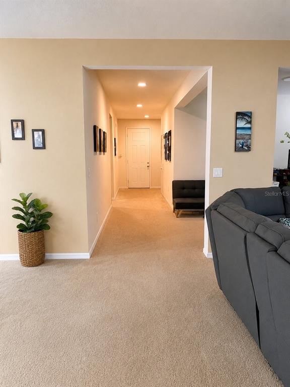 A hallway with beige carpet and walls leads to a white front door — 2809 SHELBURNE WAY, ST CLOUD, FL