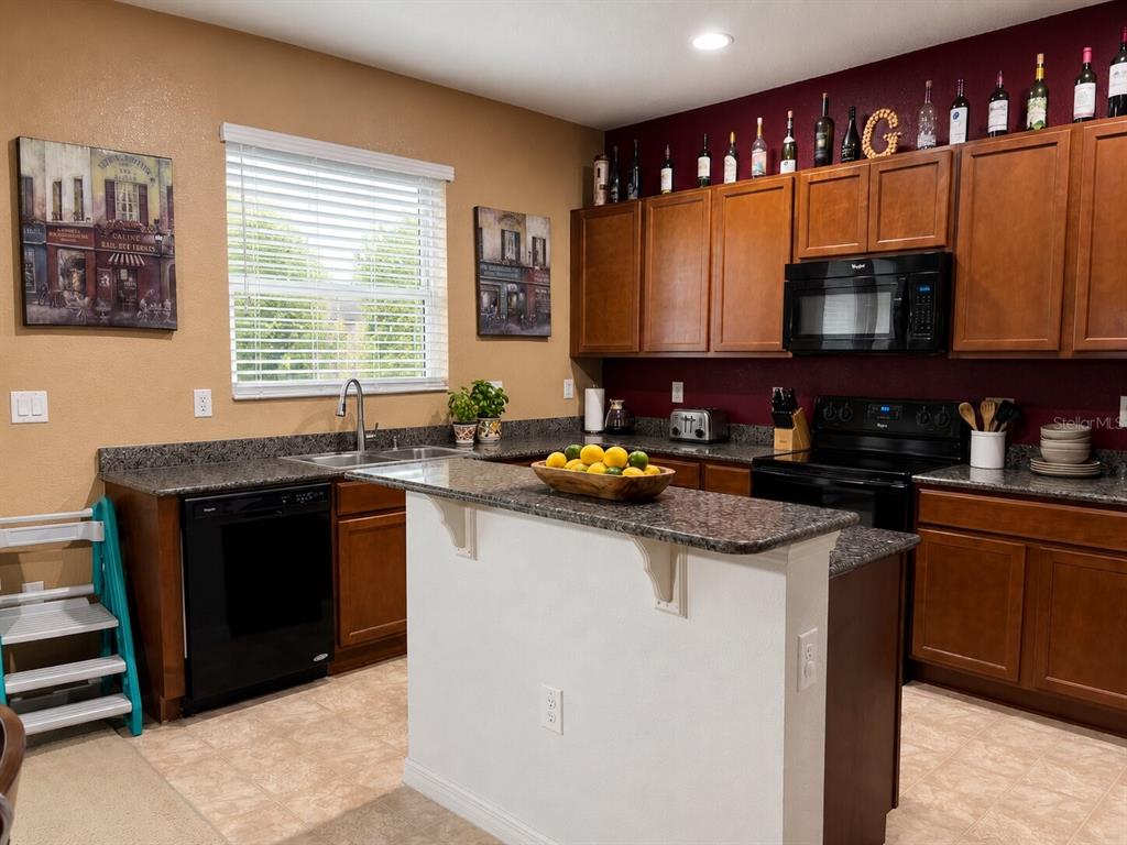 A kitchen features dark wood cabinets, granite countertops, a kitchen island, and a black appliance suite — 2809 SHELBURNE WAY, ST CLOUD, FL