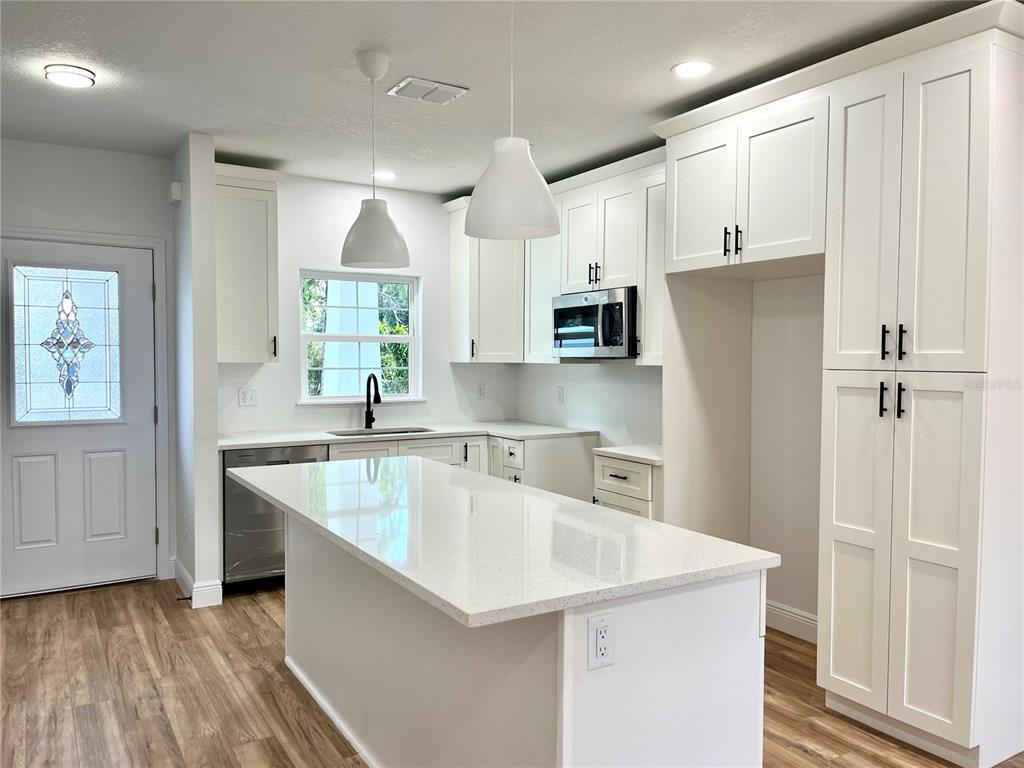 A modern kitchen features white cabinetry, a quartz-topped island, stainless steel appliances, and wood flooring — 8112 N GREENWOOD AVENUE, TAMPA, FL