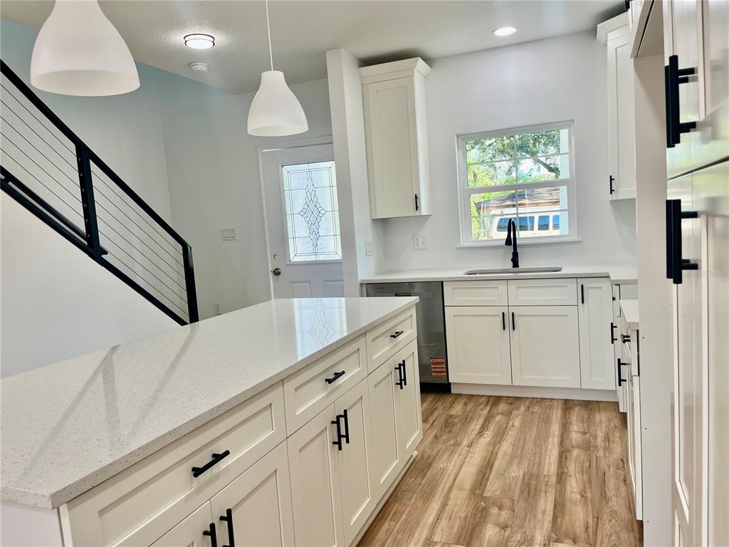 A modern kitchen features white cabinets, a quartz island, and wood-look flooring — 8112 N GREENWOOD AVENUE, TAMPA, FL