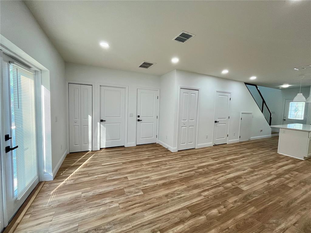 A bright living area features wood-look flooring, white walls, multiple interior doors, and a staircase — 8112 N GREENWOOD AVENUE, TAMPA, FL