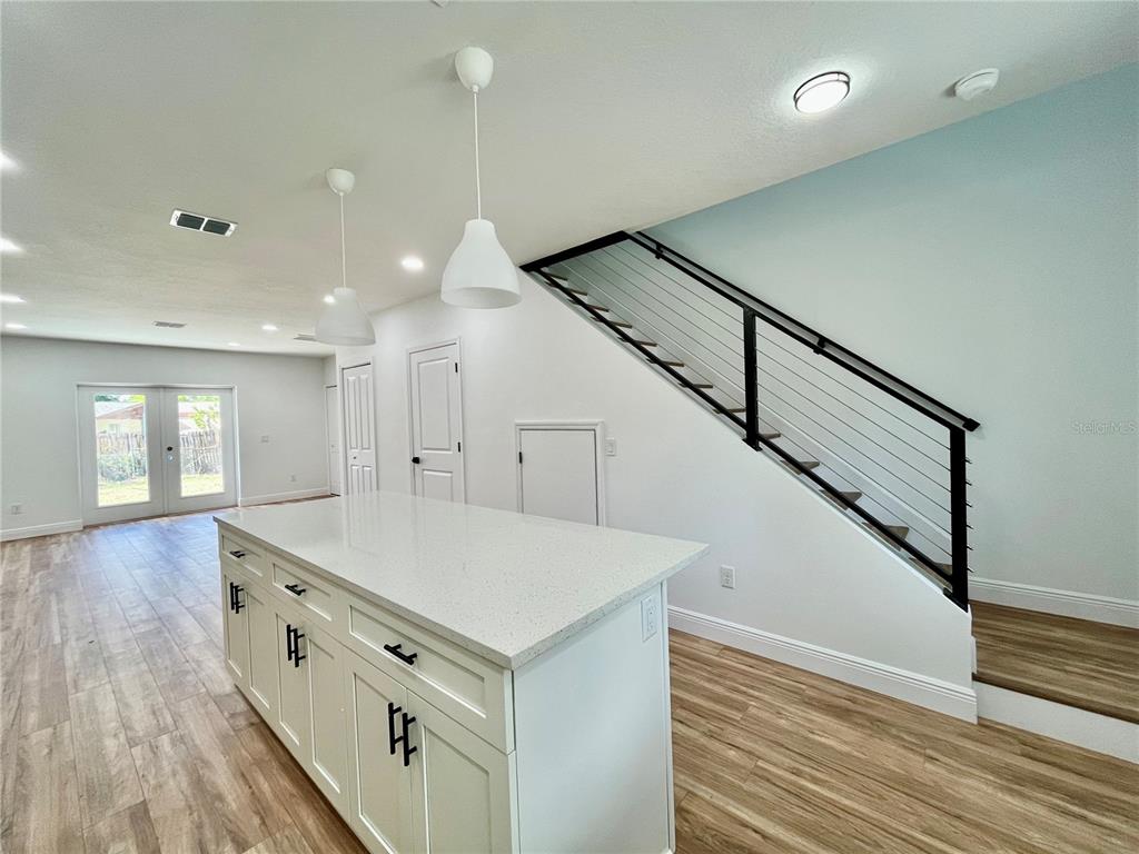 A kitchen island with white cabinets and quartz countertops sits before a staircase with railings — 8112 N GREENWOOD AVENUE, TAMPA, FL