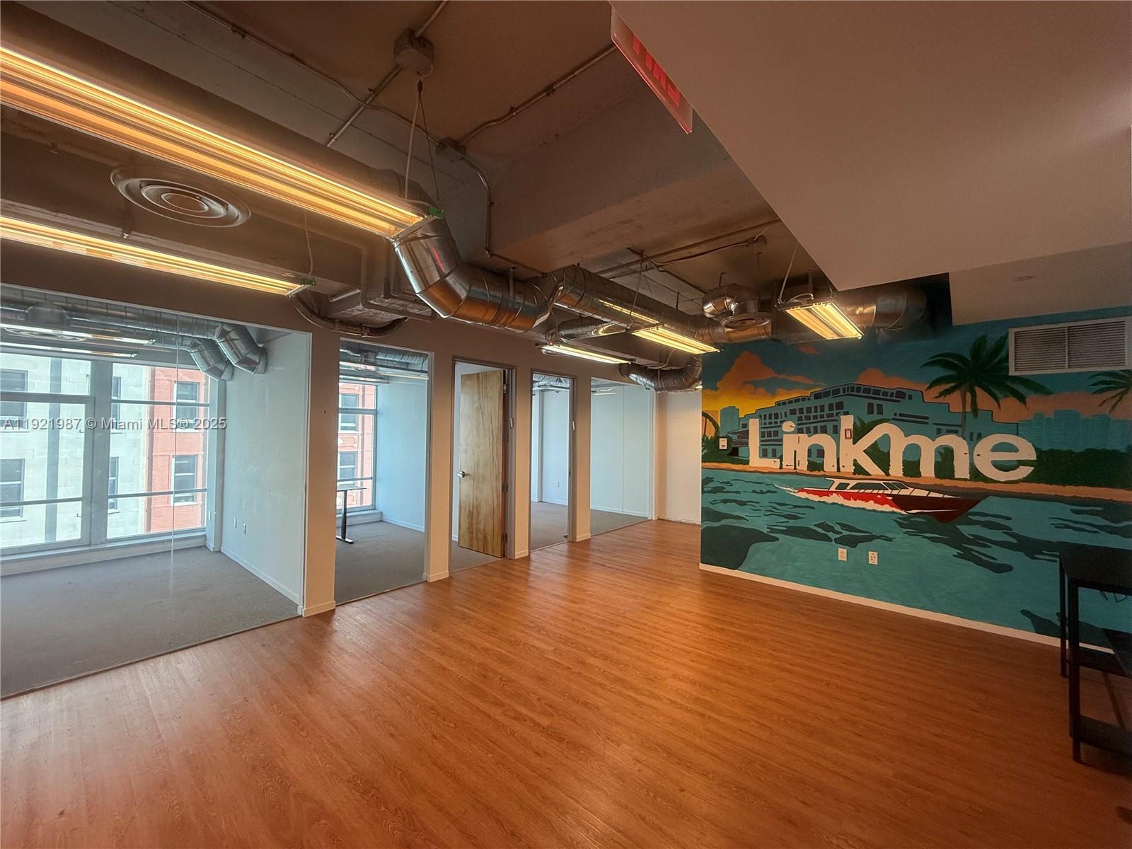 An office space features wood-look flooring, exposed ductwork, glass-walled rooms, and a mural on the wall — 14 NE 1st Ave # 800A, Miami FL 33132, MIAMI, FL