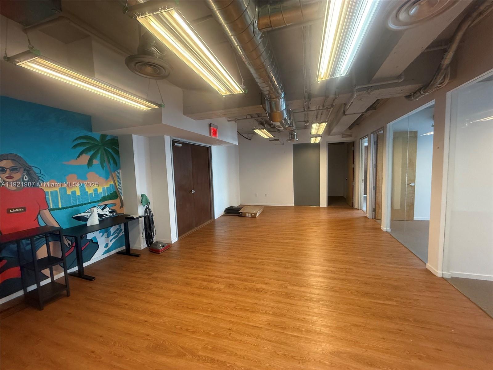 An office space features wood-look flooring, exposed ceiling ducts, and a mural on the wall — 14 NE 1st Ave # 800A, Miami FL 33132, MIAMI, FL