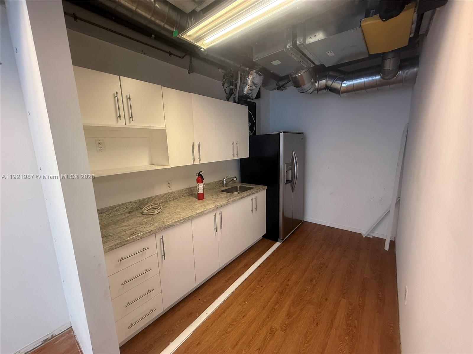 A kitchenette features white cabinets, granite countertops, a stainless steel refrigerator, and exposed ceiling ductwork — 14 NE 1st Ave # 800A, Miami FL 33132, MIAMI, FL