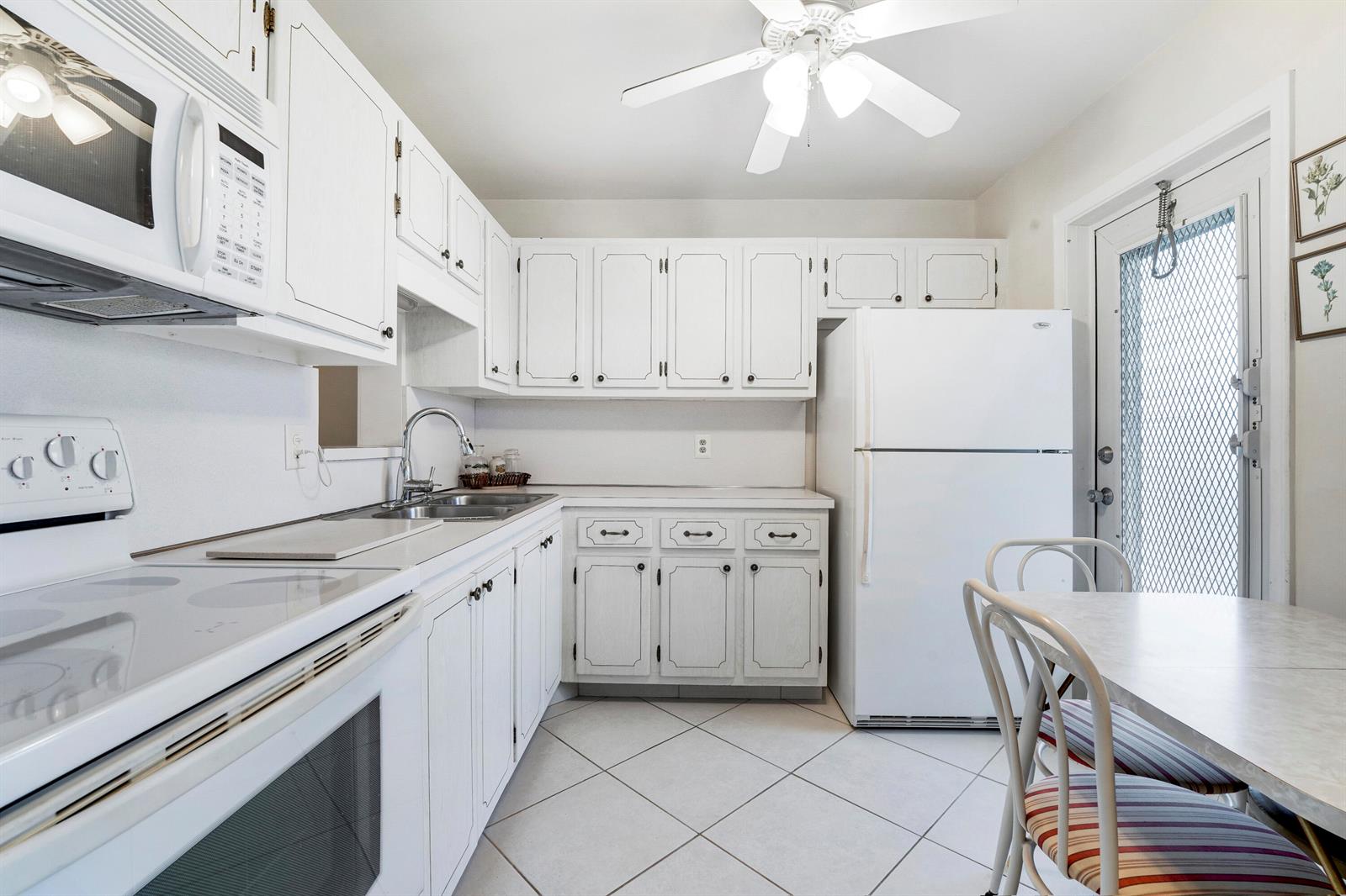 A white kitchen features white cabinets, tile flooring, a ceiling fan, and a dining area — 2132 NE 1st Way # 201, Boynton Beach FL 33435, BOYNTON BEACH, FL