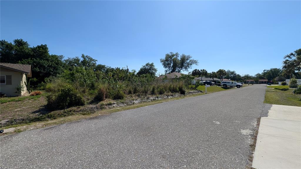 A vacant, overgrown residential lot sits along a paved street next to a house — 177 COLUMBIA ROAD, VENICE, FL
