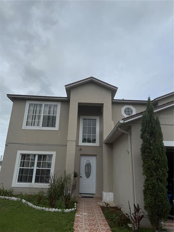 A two-story house with a tan stucco exterior, a white front door, and a tiled walkway — 517 MARICOPA DRIVE, KISSIMMEE, FL