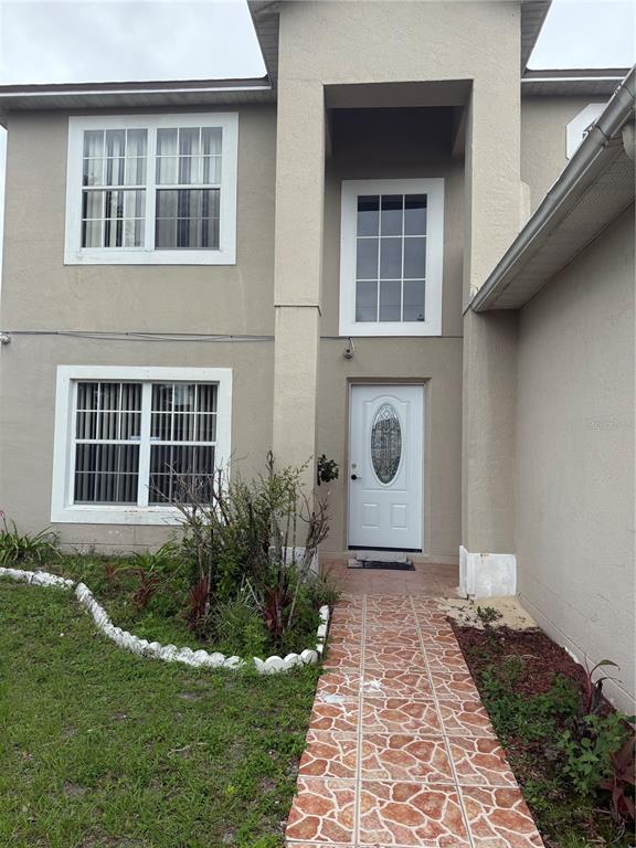 A two-story house exterior features a white front door, tiled walkway, and tan stucco siding — 517 MARICOPA DRIVE, KISSIMMEE, FL