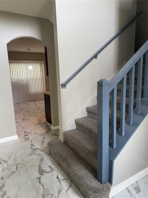 A carpeted staircase with a blue railing stands next to a tiled entryway and arched doorway — 517 MARICOPA DRIVE, KISSIMMEE, FL