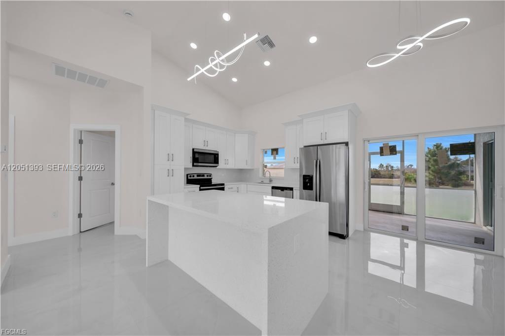 A modern kitchen features white cabinetry, a large quartz island, and stainless steel appliances — 2909 63rd St W, Lehigh Acres FL 33971, LEHIGH ACRES, FL