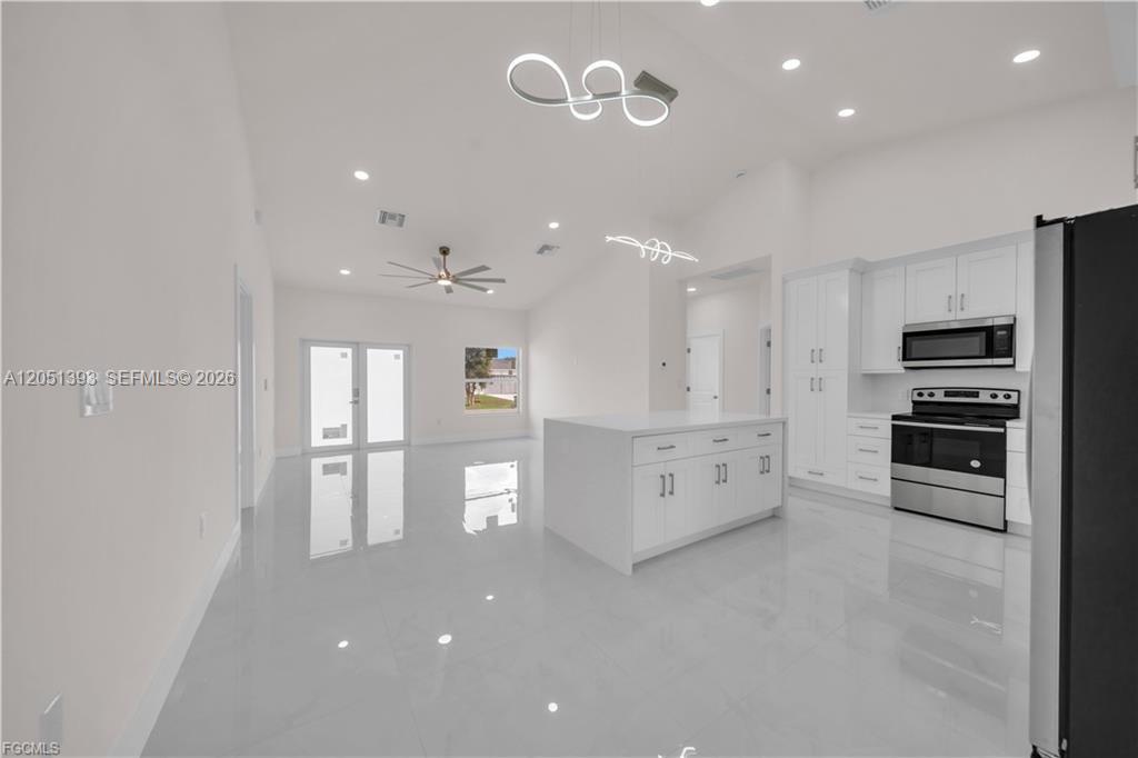 An open-concept kitchen and living area features white cabinetry, a central island, and tile flooring — 2909 63rd St W, Lehigh Acres FL 33971, LEHIGH ACRES, FL