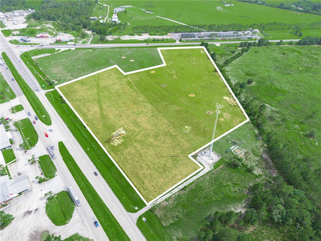 An aerial view shows a large, vacant, grassy lot outlined in white next to a highway — 7316 HWY 27, FROSTPROOF, FL