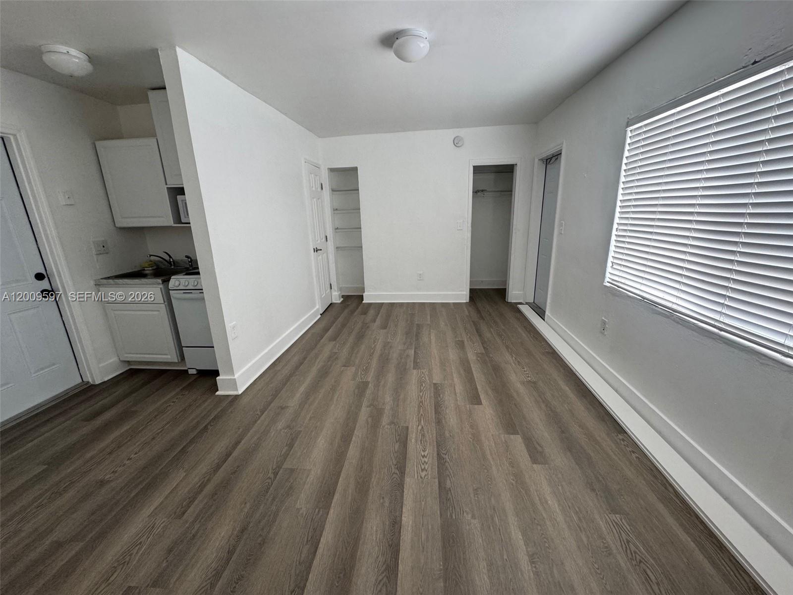 A small studio apartment features white walls, wood-look flooring, a kitchenette, and built-in shelving — 240 NW 64 str # 4, Miami FL 33150, MIAMI, FL